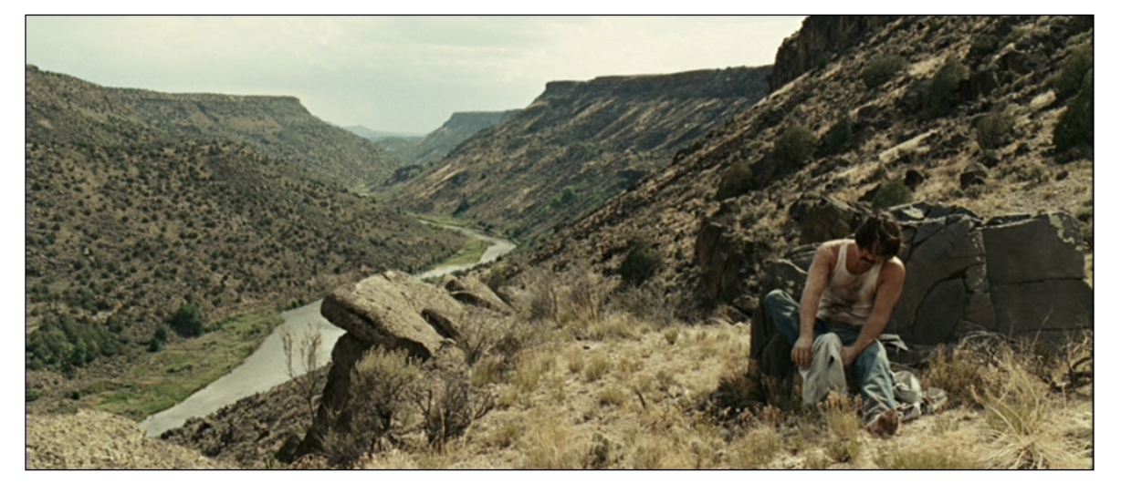 A man tugs on his boots on the side of a mountain